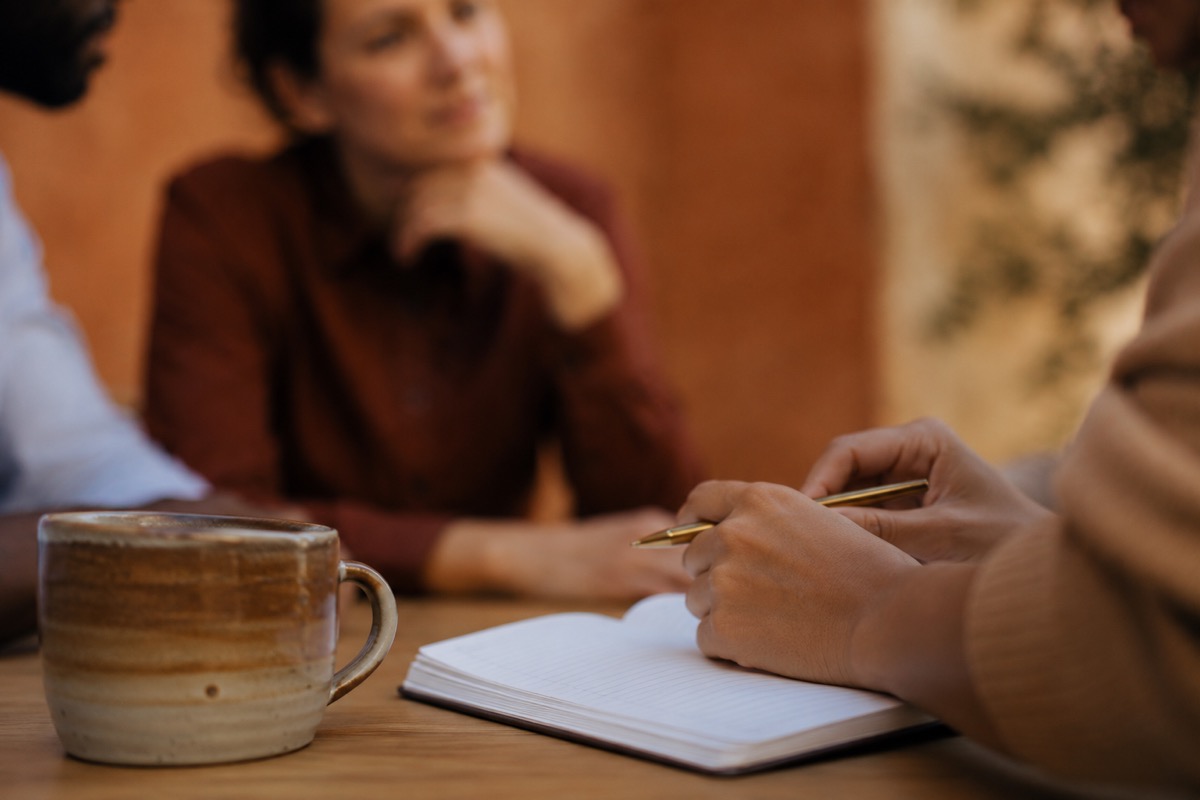 Gros plan d'une tasse de café et d'un carnet, deux praticiens en discussion.